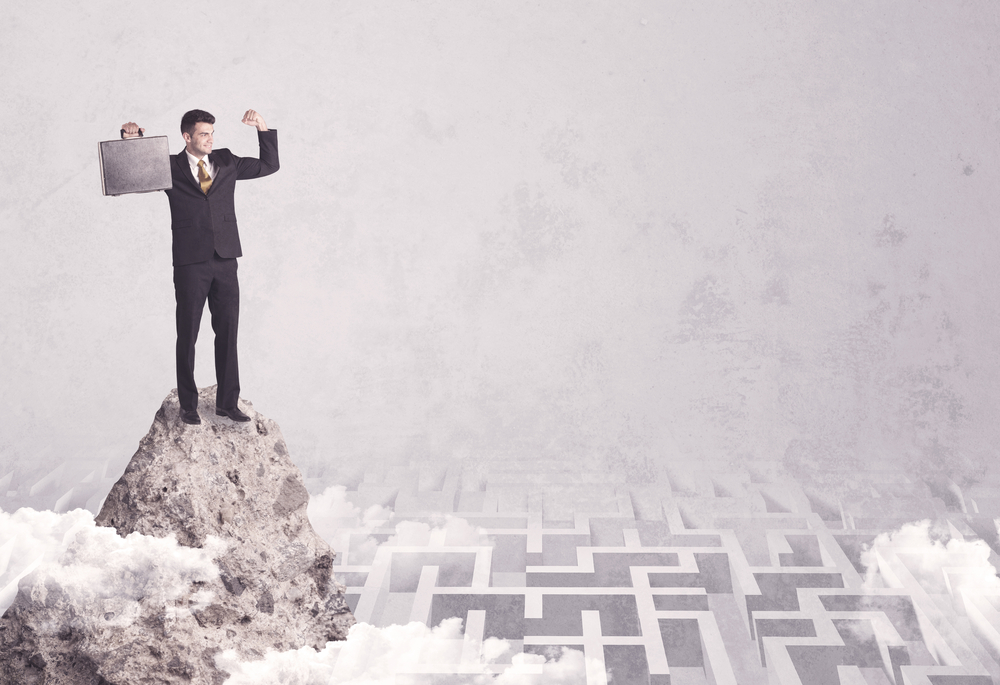 Maze is no challenge for successful businessman standing on top of a cliff as he is the best at solving problems concept